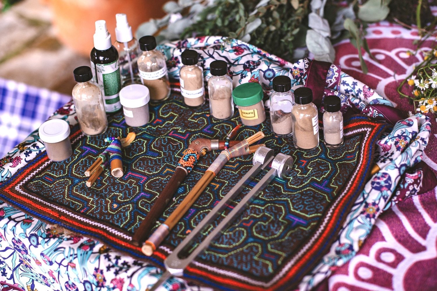 A ceremonial table laid with medicine bottles, feathers, and rapé pipes on embroidered cloth
