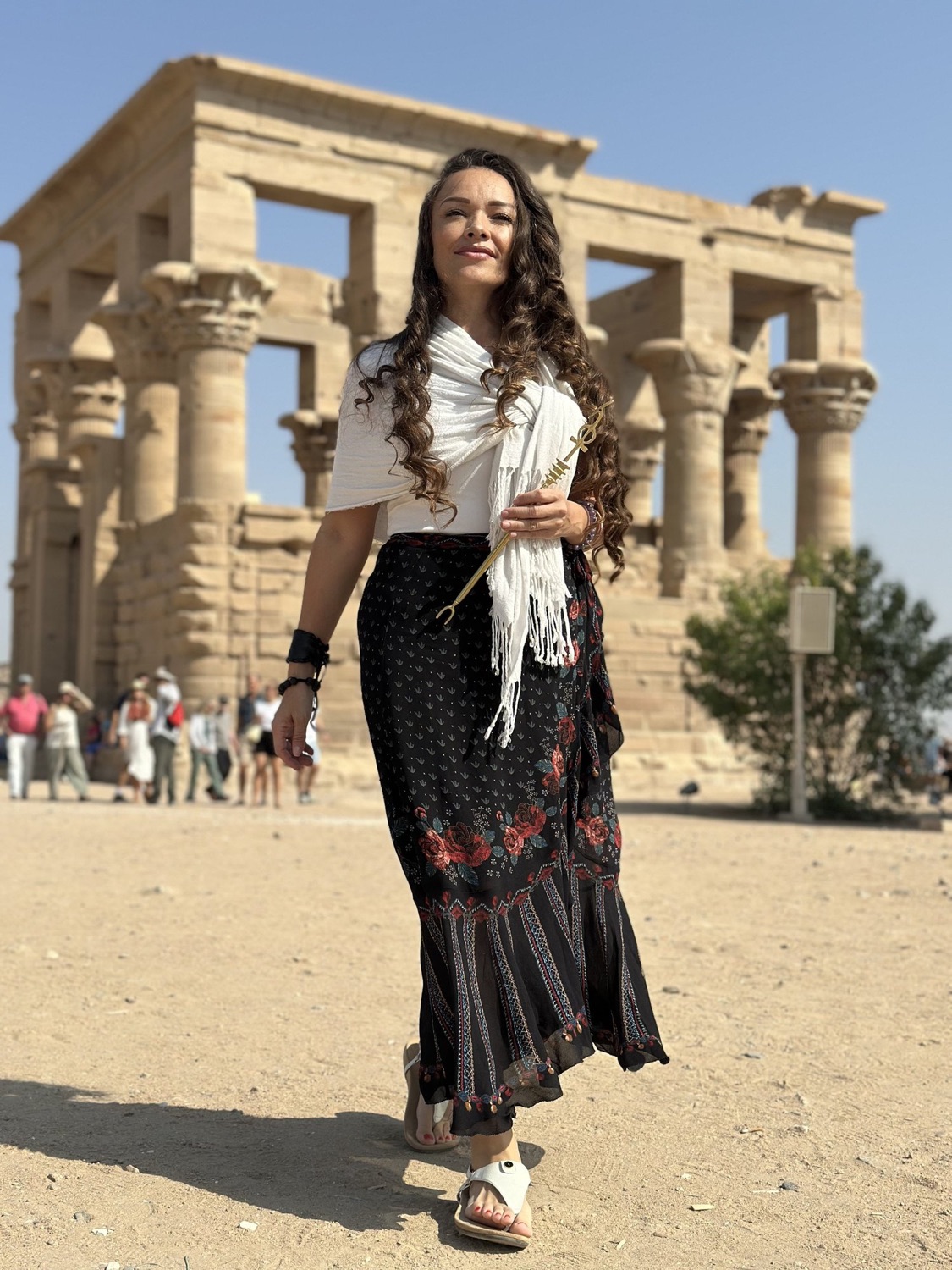 Dayana walking beside the columns of an Egyptian temple, a white shawl over her shoulder