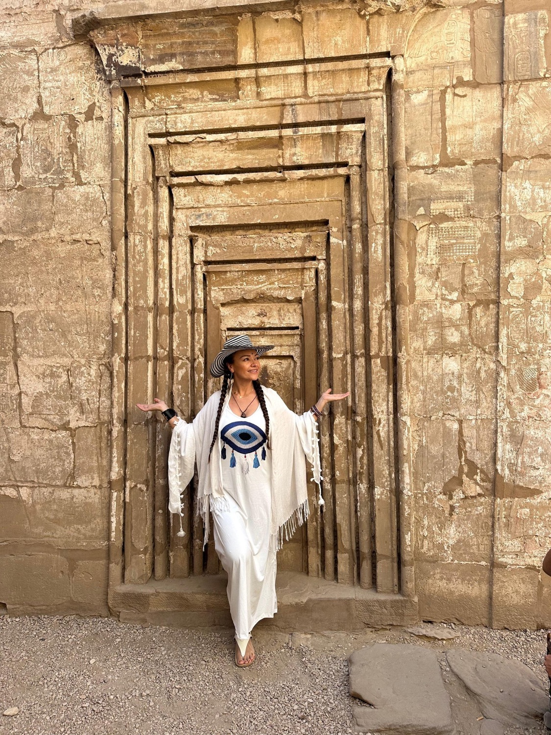 Dayana in the doorway of an Egyptian temple, arms open, wearing a white shawl marked with the eye