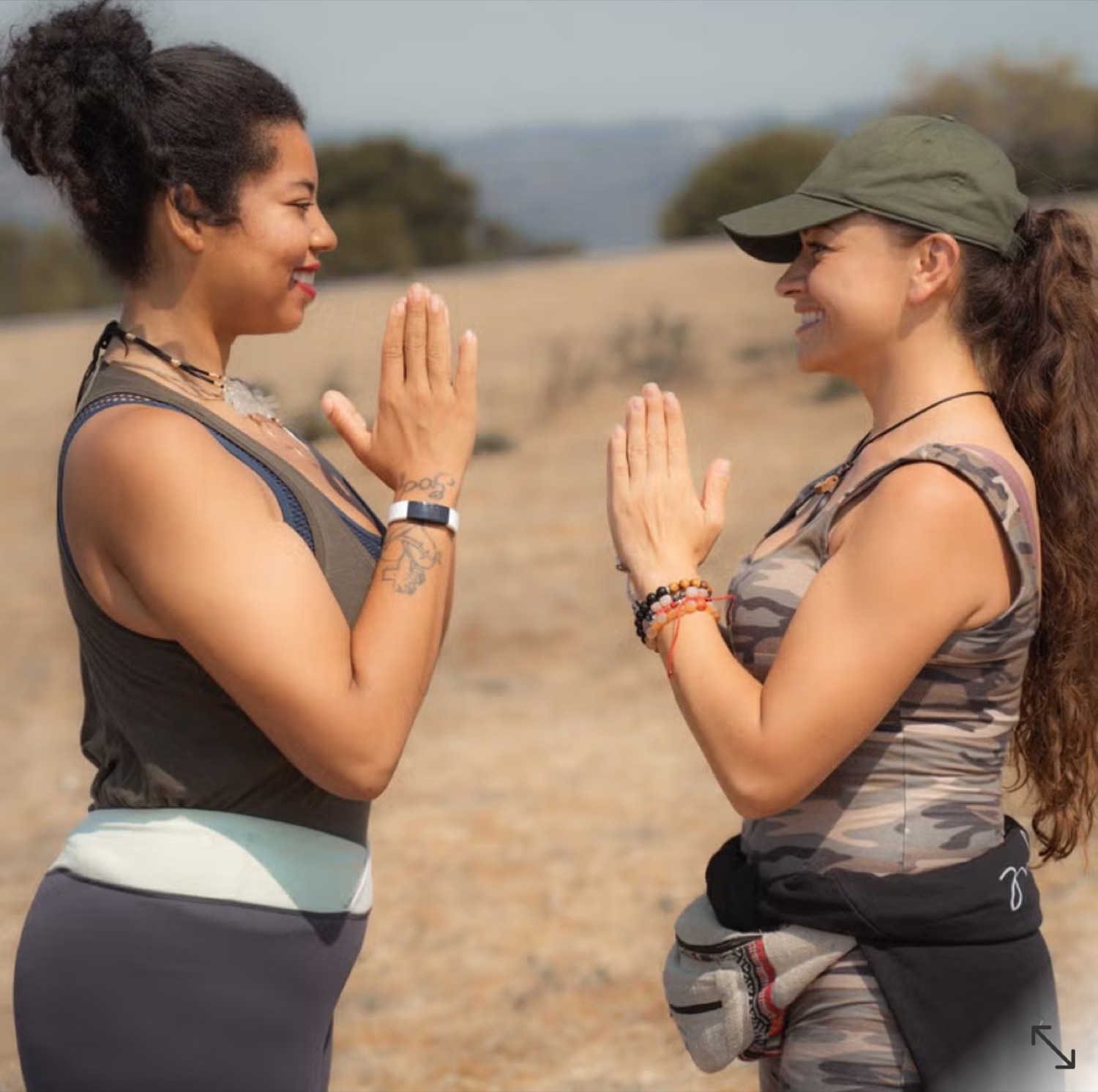 Two women facing each other outdoors, hands pressed at their hearts