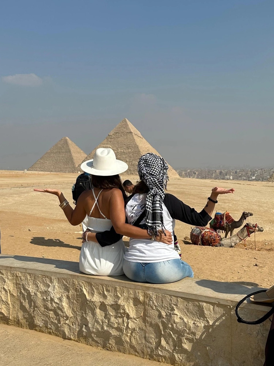 Two travellers seated before the pyramids at Giza, arms open to the horizon